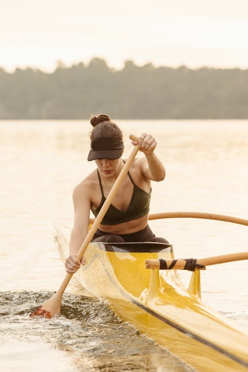 Free A woman paddles a yellow canoe across a calm lake during the day, embracing outdoor recreation. Stock Photo