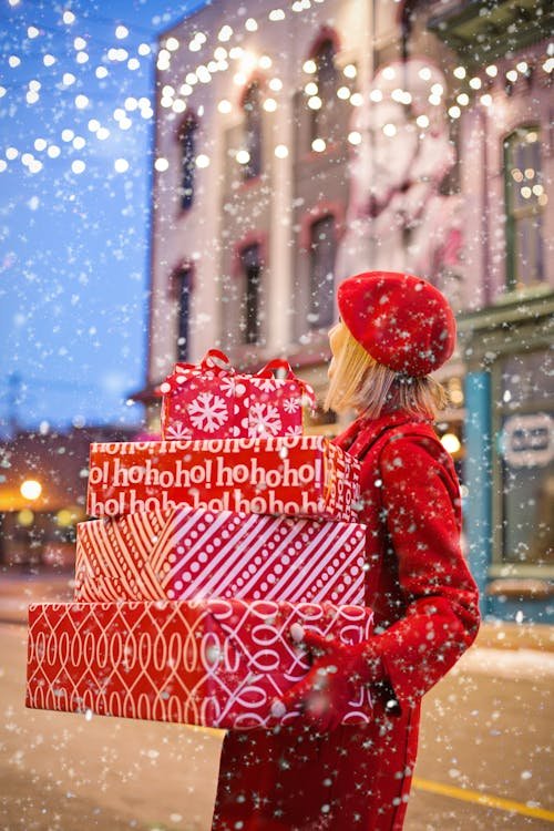 Free Woman carrying red holiday gifts in snowy city street, embracing winter festivities. Stock Photo