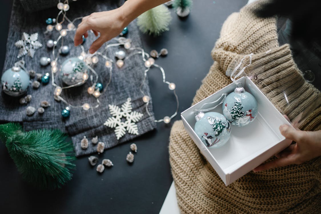 Free Hand arranging Christmas baubles amidst festive decor, setting a warm holiday atmosphere indoors. Stock Photo