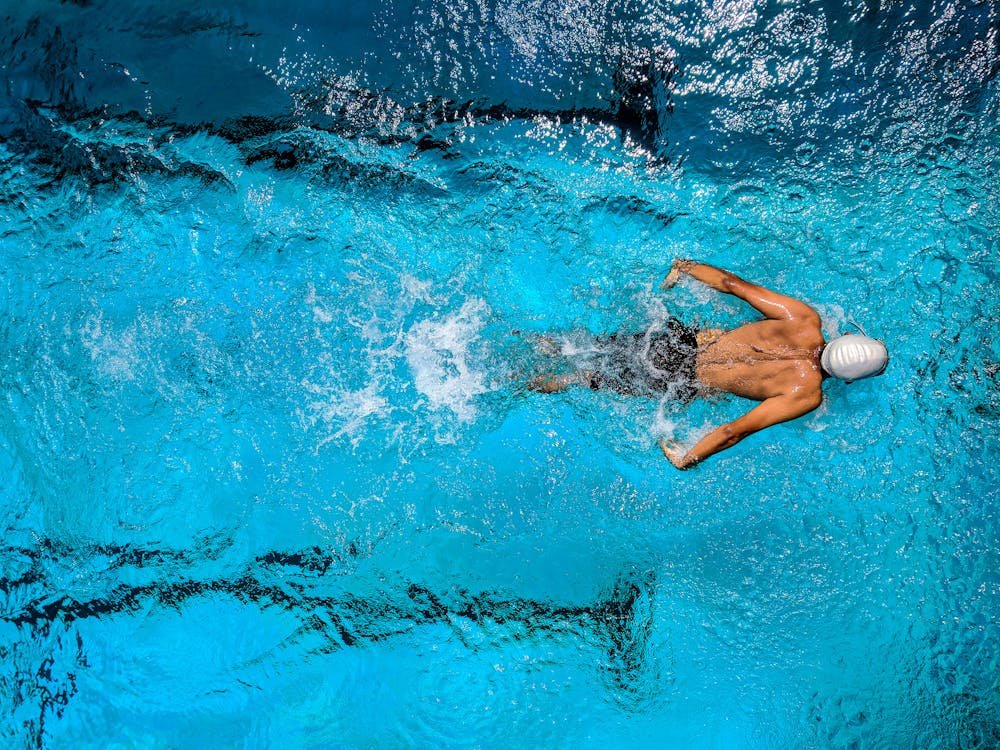 Free Top view of a swimmer wearing a cap, performing a front crawl stroke in a clear blue swimming pool. Stock Photo