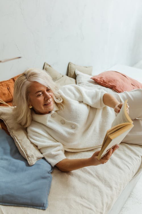 Free Elderly woman in a cozy setting enjoying leisure reading while lying on a bed. Stock Photo