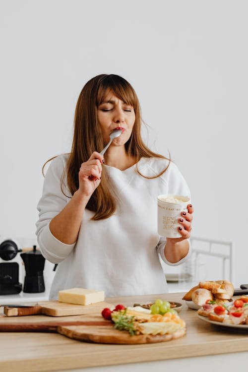 Free Woman savoring ice cream while cooking in a modern kitchen. Perfect lifestyle imagery. Stock Photo