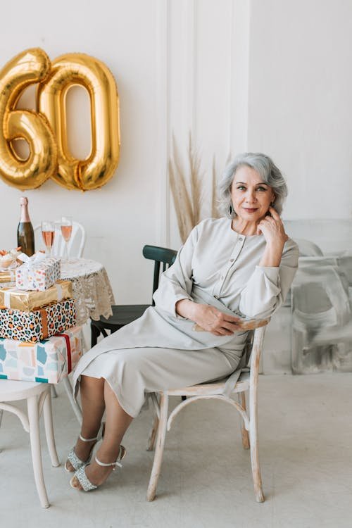 Free Senior woman enjoying her 60th birthday celebration with presents and champagne indoors. Stock Photo