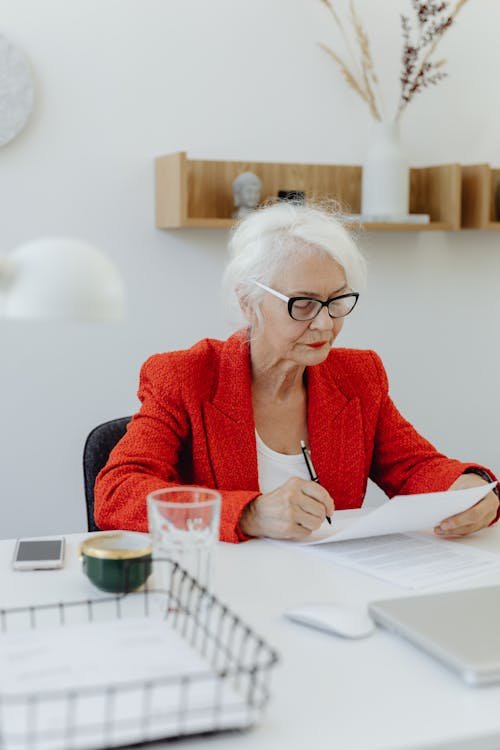 Free Elderly woman in a red blazer working at a desk, exuding professionalism and focus. Stock Photo